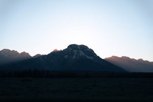 Evening sun behind Mount Moran, Wyoming, with sun-kissed peaks and a dark, tranquil foreground.